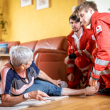 Rotkreuz-Sanitäter helfen einer Dame, nachdem sie auf ihrem Rufhillfe-Armband den Notrufknopf gedrückt hat.