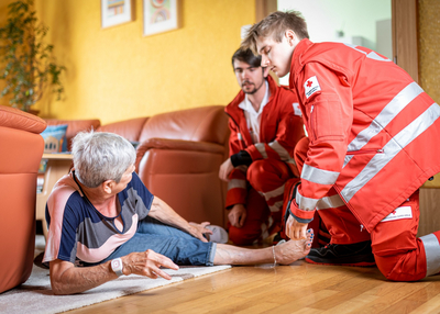 Rotkreuz-Sanitäter helfen einer Dame, nachdem sie auf ihrem Rufhillfe-Armband den Notrufknopf gedrückt hat.