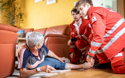 Rotkreuz-Sanitäter helfen einer Dame, nachdem sie auf ihrem Rufhillfe-Armband den Notrufknopf gedrückt hat.