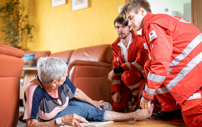 Rotkreuz-Sanitäter helfen einer Dame, nachdem sie auf ihrem Rufhillfe-Armband den Notrufknopf gedrückt hat.