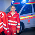 Rotkreuz-Mitarbeiter in Uniform vor einem Rettungswagen hat seine passende Jacke in der Hand.