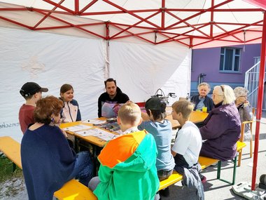 Eine Gruppe von Menschen sitzt um einen Tisch unter einem Zelt.