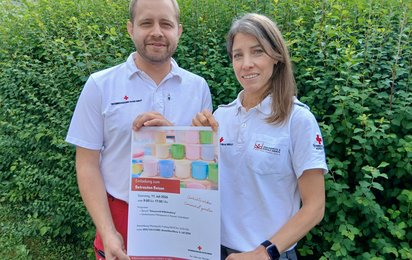 Rotkreuz-Mitarbeiter mit Veranstaltungsplakat für das Betreute Reisen