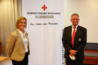 Neue Ortsstellenleiter Mag. Tanja Weigl und Ortsstellenleiter außer Dienst Holger Oppenborn vor dem Rotkreuz-Roll-Up