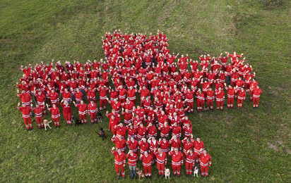 Kreuz aus Rotkreuz-Mitarbeitern stehen im Kreuz zusammen auf einer Wiese