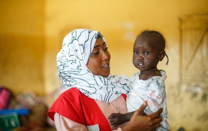 Helferin des Sudanesischen Roten Halbmonds im Sudan mit Kind auf dem Arm