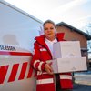 Eine Zuhause-Essen-Mitarbeiterin steht mit Essenspaketen vor einem Rotkreuz-Auto