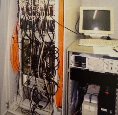 Serverschrank und viele Kabel und ein typischer PC der Anfang der 2000er Jahre.