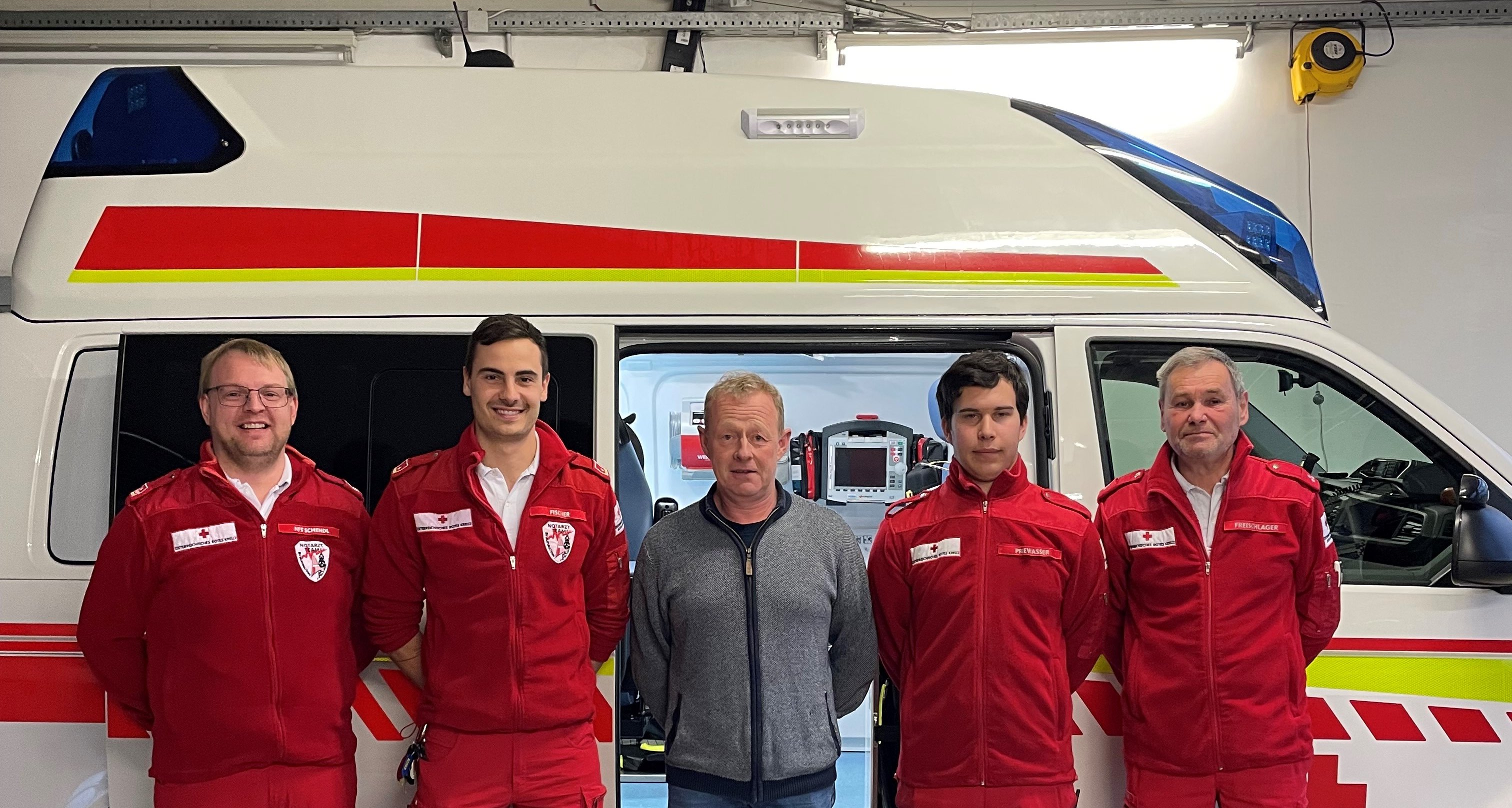 ein Mann wird von je 2 Rettungssanitäter flankiert, sie stehen vor einem Rettungsauto