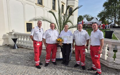 Elisabeth Hafner mit Urkunde, Ehrenzeichen und Blumen gemeinsam mit Kollegen des Roten Kreuzes Schwechat beim Schwechater Stadtfest.
