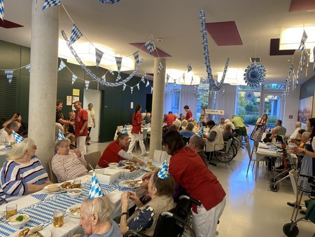 Der Speisesaal des Seniorenwohnhauses Hallein, dekoriert in Weiß-Blau mit Bewohner:innen an Tischen und Pflegepersonen.