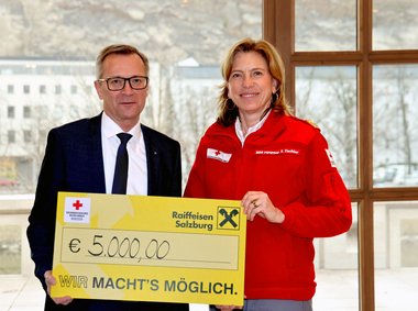 Heinz Konrad, links, Generaldirektor Raiffeisenverband Salzburg, bei der Spendenübergabe an Sabine Tischler, Landesgeschäftsführerin RK Salzburg. Sie halten gemeinsam einen großen Scheck mit der Spendensumme in der Hand.
