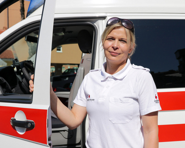 Das Bild zeigt die Sichere Einsatzfahrerin Sigrun der Rotkreuz-Bezirksstelle Graz-Stadt an der Fahrertür eines Rettungswagens.