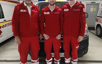 VAtertag - © Credit: OÖRK / Urfahr-Umgebung Vater Klaus mit seinen beiden Söhnen Leo und Felix, alle drei in Rotkreuz-Uniform, abgebildet vor einem SEW in der Rettungsgarage.