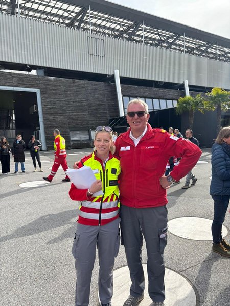 Zwei Mitarbeiterinnen des Roten Kreuzes vor dem Stadion des FC Red Bull Salzburgs. Links steht eine Frau in Rotkreuz-Uniform mit gelber Weste, rechts ein Mann in Rotkreuz-Uniform mit roter Jacke.