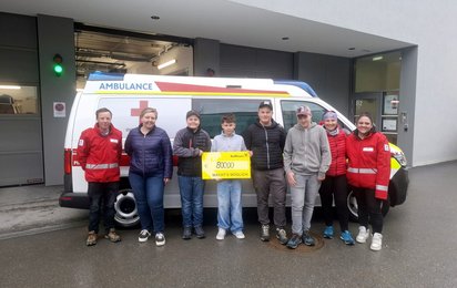 Eine Gruppe von Menschen steht vor einem Rettungswagen. Eine Person hält einen großen Scheck in Händen.