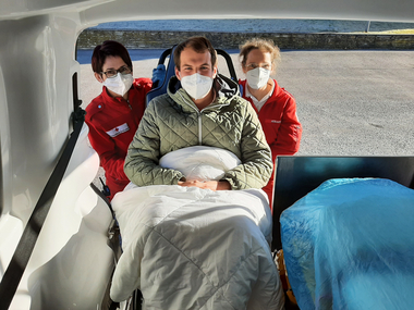 2 Rettungssanitäterinnen schieben einen Patienten am Tragsessel in das Rettungsauto
