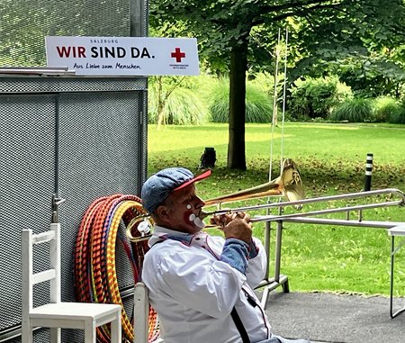 Ein Clown sitzt auf einem Sessel und spielt Posaune