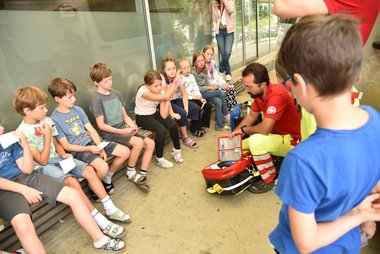 Kinder sitzen im Kreis und bekommen den Inhalt des Notfallrucksacks vorgestellt
