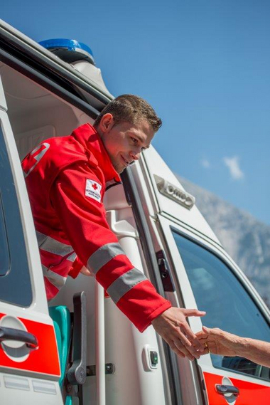 Ein Rettungssanitäter reicht vom Rettungsauto heraus einem Menschen die Hand. Den Menschen selbst sieht man nicht