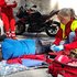 Junges Mädchen in Rot Kreuz Uniform und Überwurfweste kniet rechts neben Patienten in Stabiler Seitenlage