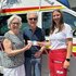 Eine Rotkreuz-Mitarbeiterin überreicht eine Hitzebuddy-Freecard älternen Menschn vor einem Rettungsauto.