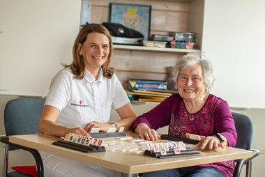 Eine freiwillige RK-Mitarbeiterin in weißem Shirt spielt mit einer älteren Dame Rumy Cub.