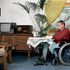 Pflege daheim - leicht(er) gemacht. Mit Pflegemittel für daheim wie z. B. mit einem Rollstuhl ist Betroffenen und ihren Familien geholfen. Am Bild sitzt ein Mann im Rollstuhl an einem Tisch und liest ein Buch.