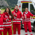 Vier Mitarbeiter des Roten Kreuzes Tirol in Roter Uniform stehen am Feld mit dem Rettungsauto im Hintergrund und heben ihren Daumen in die Höhe