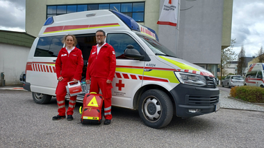 RK-Mitarbeiterin Isabell und RK-Mitarbeiter Alois Höbart stehen in Uniform vor dem Rettungsauto