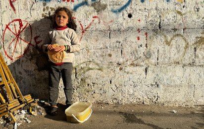 Mädchen in Gaza steht an einer Wand und hält ein Brot in der Hand