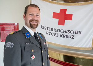 Ing. Christoph Berghofer - Bezirksstellenleiter - trägt seine Ausgangsuniform und steht vor einer Rotkreuz-Standarte.