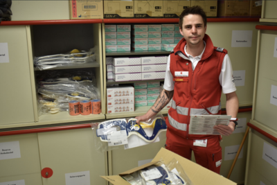 Freddy Lechner steht in Rotkreuz-Uniform in einem Lager voller Sanitätsmaterialien.