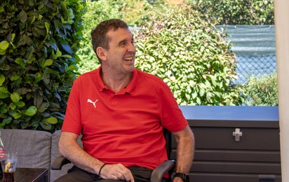 Thomas Hansa sitzt am Tisch mit seinem Rollstuhl und lächelt.