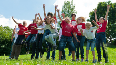Jugend - © RK NÖ/Ulrich Moshammer Kindergruppe springt auf einer Wiese.