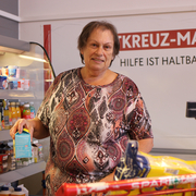 Eine Frau steht im Rotkreuz-Markt vor der Kühlvitrine und wählt mit Bedacht, Lebensmittel aus.