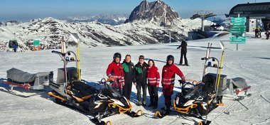 Gruppenfoto mit zwei Skidoos im Skigebiet Wildkogel im Bereich der Pfeifferköpfl-Bahn. Zu sehen sind von links nach rechts: Stefan Innerhofer (Notfallsanitäter), Rudi Göstl (Geschäftsführer Bergbahnen Wildkogel), Gerhard Enzinger (Betriebsleiter Bergbahnen Wildkogel), Isabella Pernthaner-Schneider (Bezirksgeschäftsführerin Rotes Kreuz Pinzgau), Alexander Gandler (Rettungssanitäter)