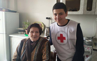 iris_armenian-red-cross.jpg - © Armenian Red Cross Ein junger Freiwilliger des Armenischen Roten Kreuzes steht neben einer älteren Dame und hält die Hand auf ihrem Rücken. Beide lächeln in die Kamera.