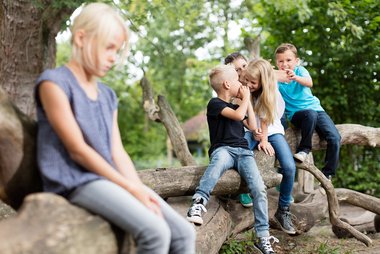 Ein ein von einer Gruppe lachender Kinder abseits sitzendes Kind wirkt traurig.