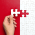 Eine Hand gestaltet ein Rot-weißes Puzzle und fügt gerade ein weißes Teil hinzu