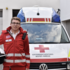 Maximilian Zarfl steht in Rotkreuz-Uniform vor einem Rettungswagen und hält dabei einen Schutzhelm unter dem Arm. An seiner linken Brust ist ein Funkgerät sichtbar.
