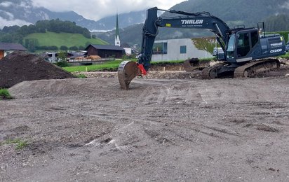 Bagger auf einem Baugrundstück mit Kirche Wiesing im Hintergrund