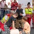 Ein Kind reanimiert eine Wiederbelebungspuppe, daneben ein weiteres Kind, im Hintergrund Sanitäter:innen, Zuschauer:innen und der Initiator des Weltrekordversuchs Dr. Ernst Toferer