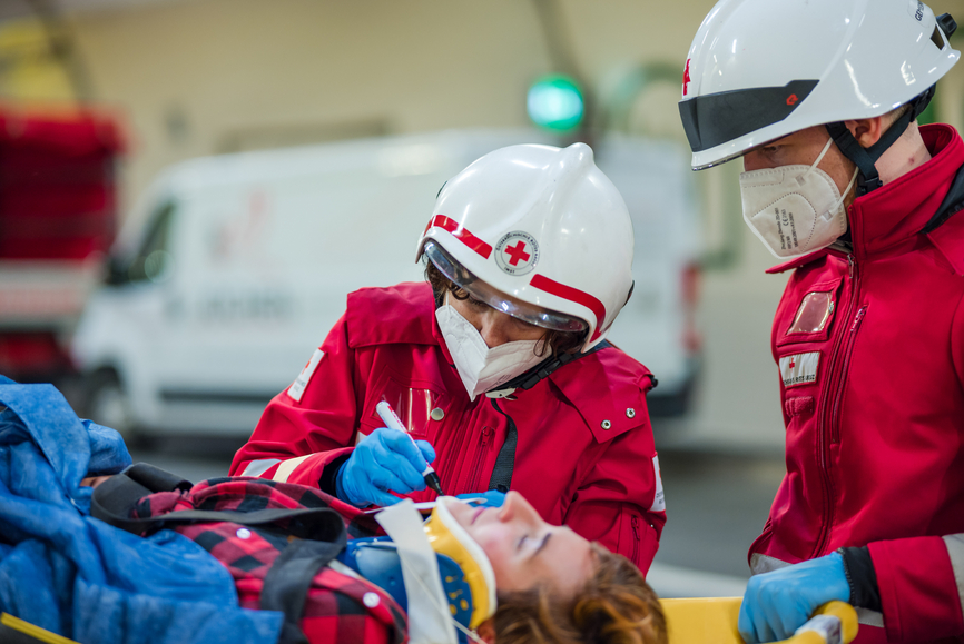 Sanitäter:in - © Rotes Kreuz Tirol, Berhard Stolz zu sehen ist eine Sanitäterin, der von einem anderen Sanitäter assistiert wird, beide versorgen sie gerade einen Menschen, der auf der Trage liegt und eine Halskrause trägt