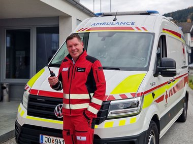 Markus Moser steht ihn einer Rotkreuz-Uniform vor einem Rettungswagen und hält ein Funkgerät in der Hand