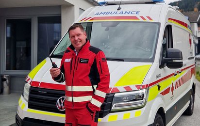 Markus Moser steht ihn einer Rotkreuz-Uniform vor einem Rettungswagen und hält ein Funkgerät in der Hand