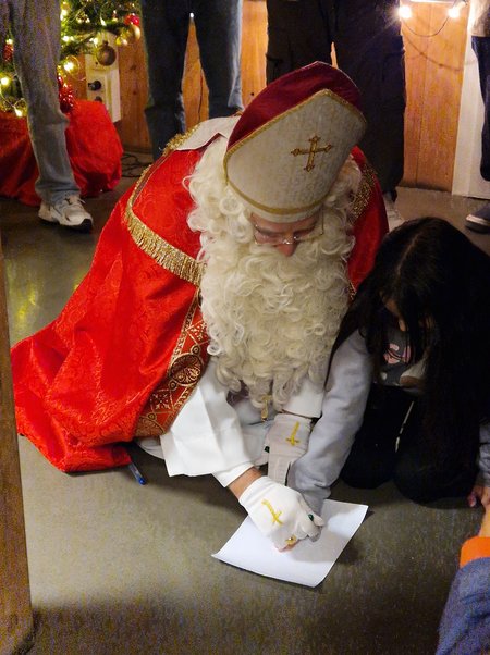 Der Nikolaus kniet mit einem Kind am Boden und zeichnet auf einem Blatt Papier
