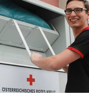 Junger Mann mit schwarzen Shirt und Brille wirft eine Kleidertasche in den Sammelcontainer des Roten Kreuzes