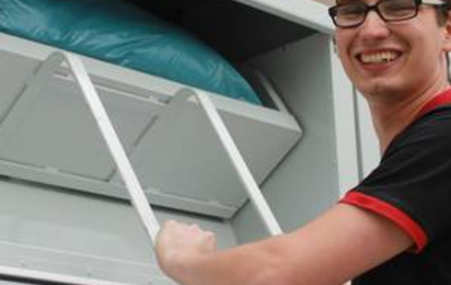 Junger Mann mit schwarzen Shirt und Brille wirft eine Kleidertasche in den Sammelcontainer des Roten Kreuzes