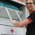 Junger Mann mit schwarzen Shirt und Brille wirft eine Kleidertasche in den Sammelcontainer des Roten Kreuzes